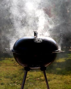 Capture of a smoking barbecue grill outdoors, emitting steam on a bright sunny day.