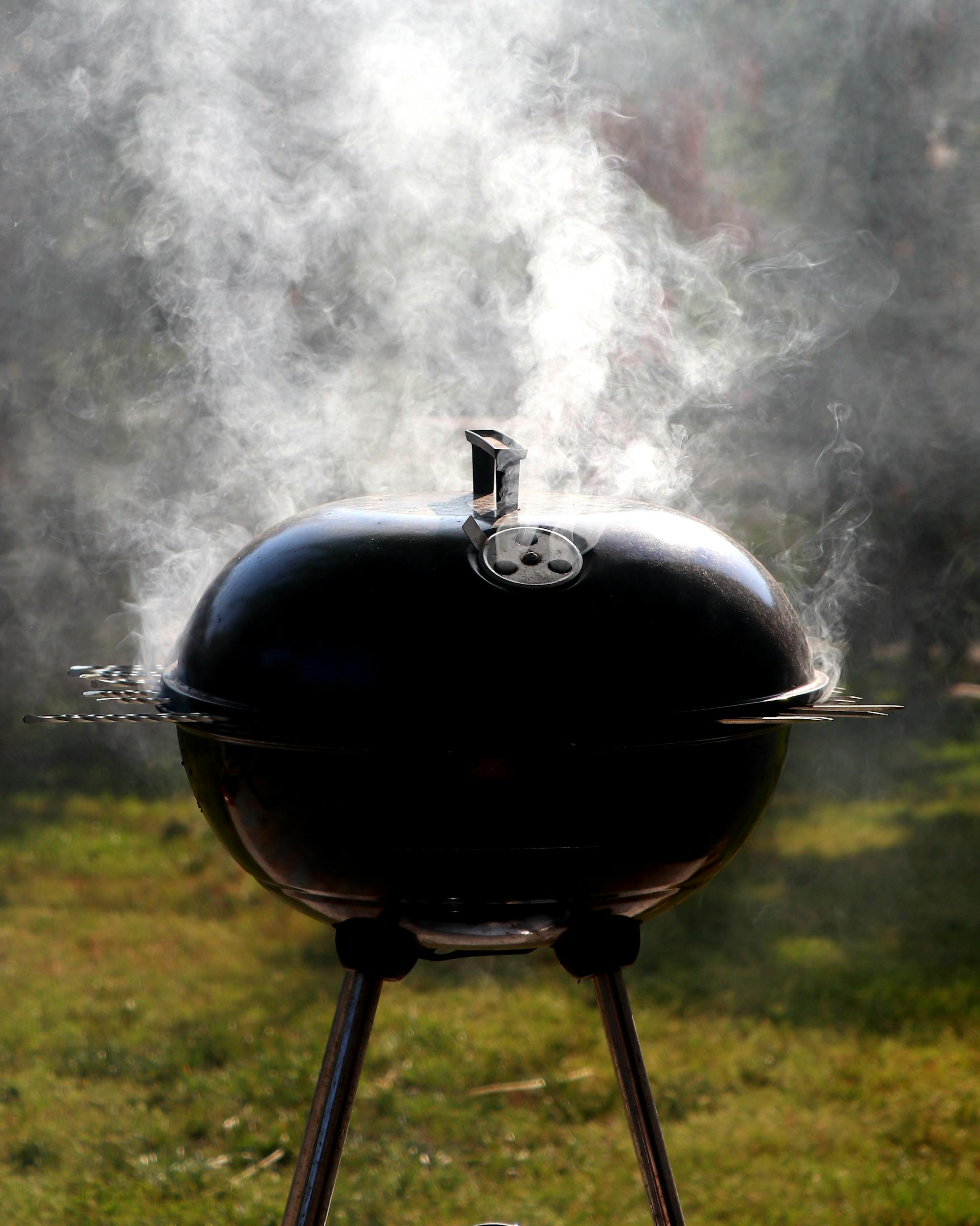Capture of a smoking barbecue grill outdoors, emitting steam on a bright sunny day.