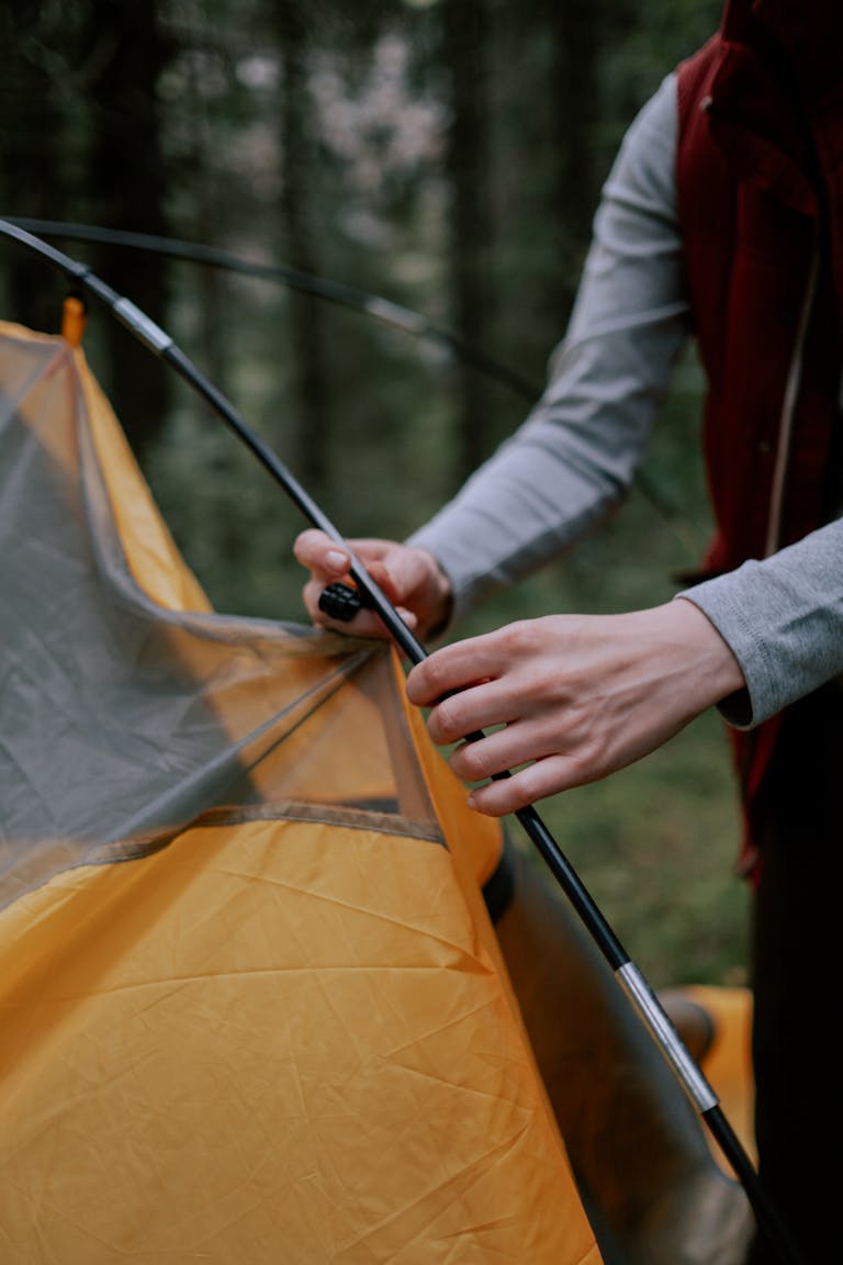 Hands assembling a tent in a forest, perfect for camping enthusiasts.