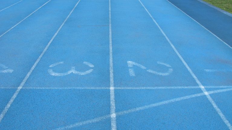 Close-up view of a blue athletics track with white lane numbers and markings.